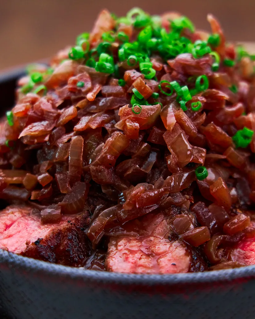 Sliced steak over rice under a pile of red wine onions and green onion