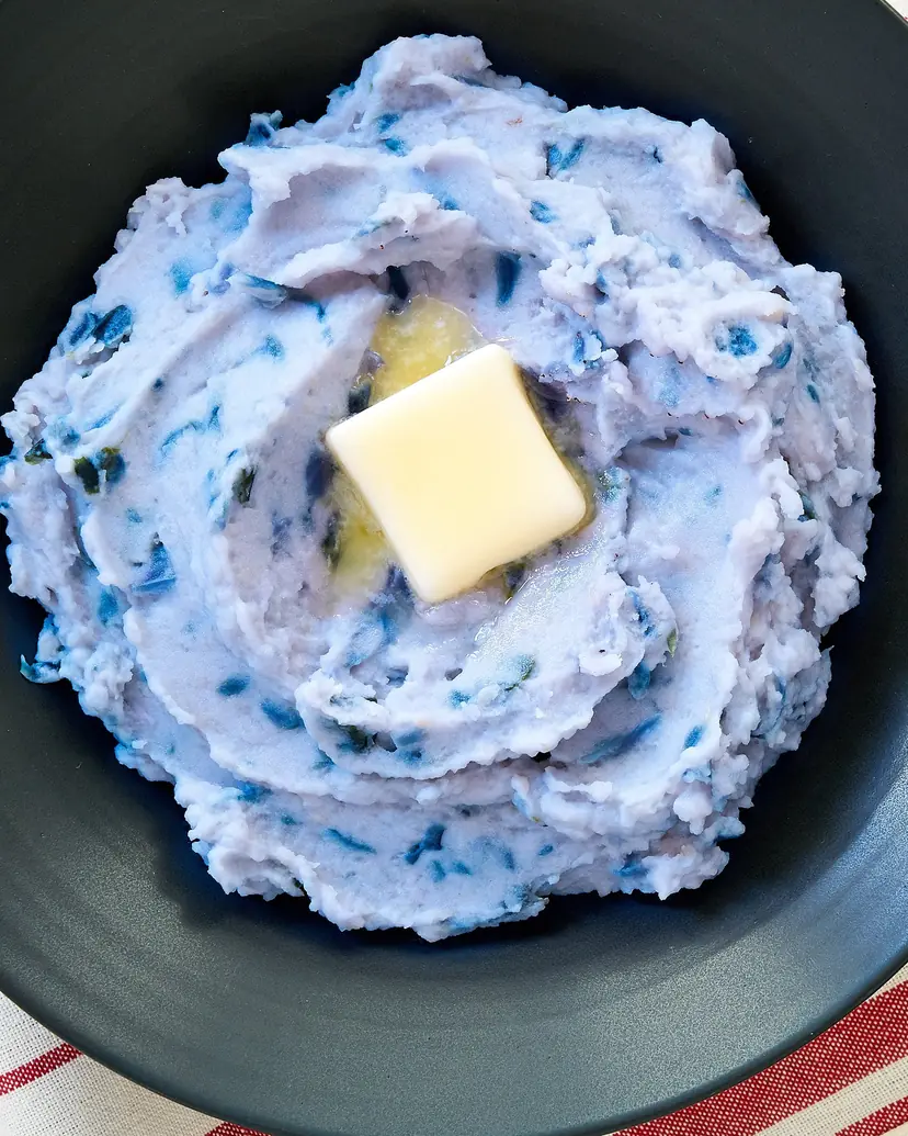 Pale blue mashed potatoes with a pat of butter in a black bowl