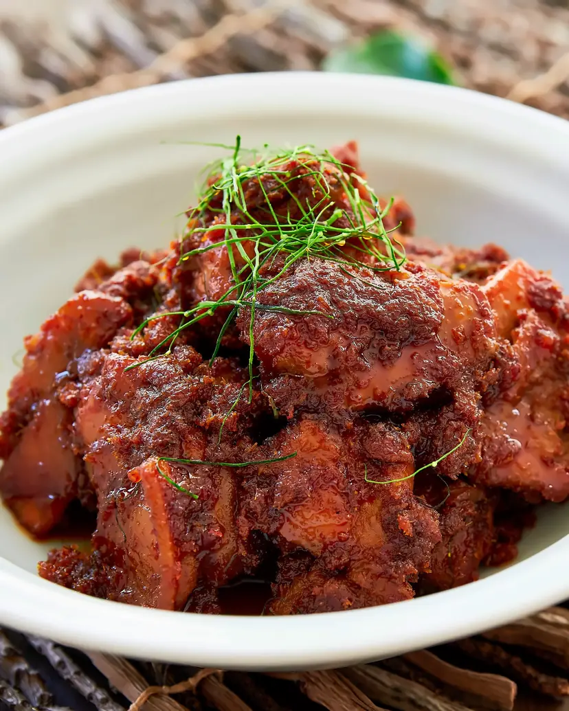Chicken rendang in a thick spiced coating, topped with shredded lime leaf, in a white bowl