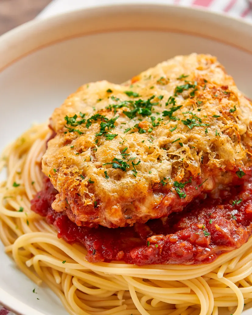 A crisp parmesan-crusted chicken thigh with parsley on tomato sauce and spaghetti