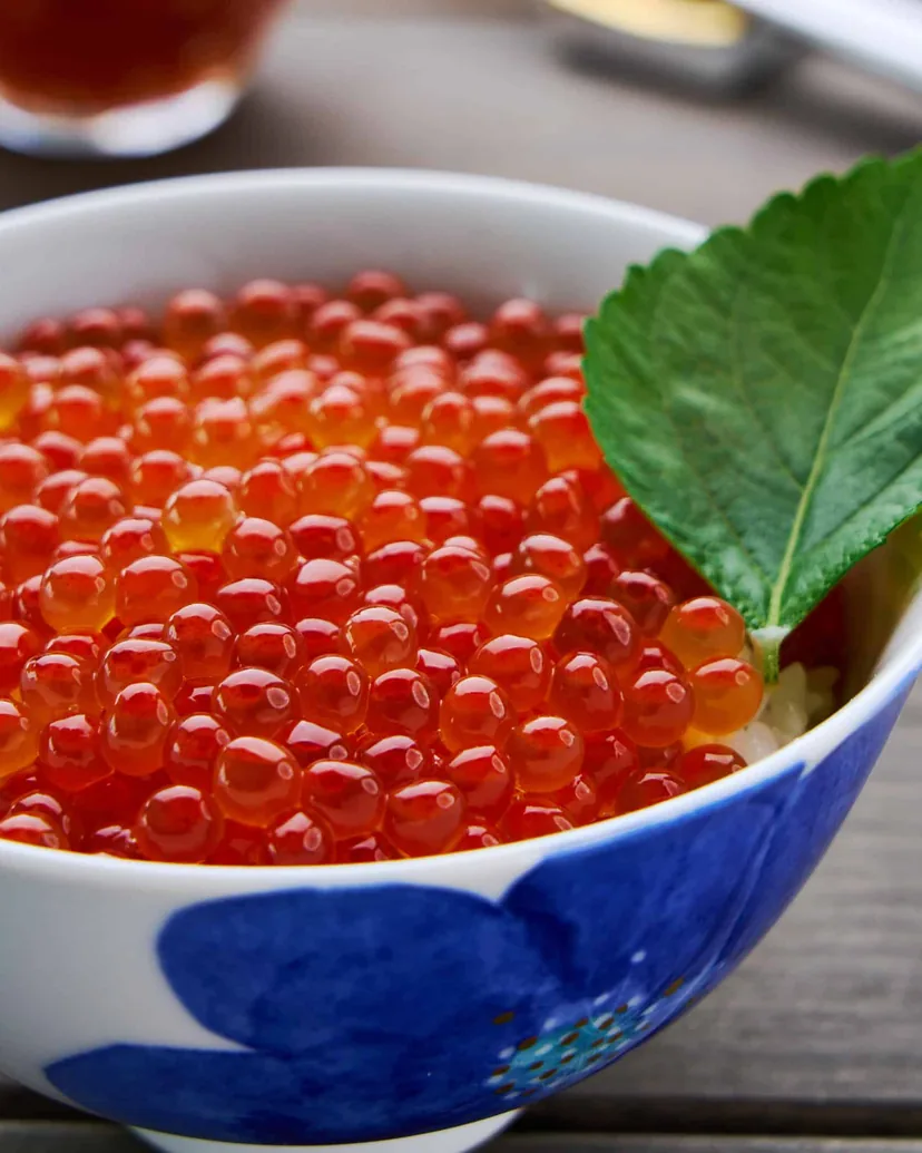 A blue and white bowl of rice heaped with glistening salmon roe, with a shiso leaf tucked in at the side