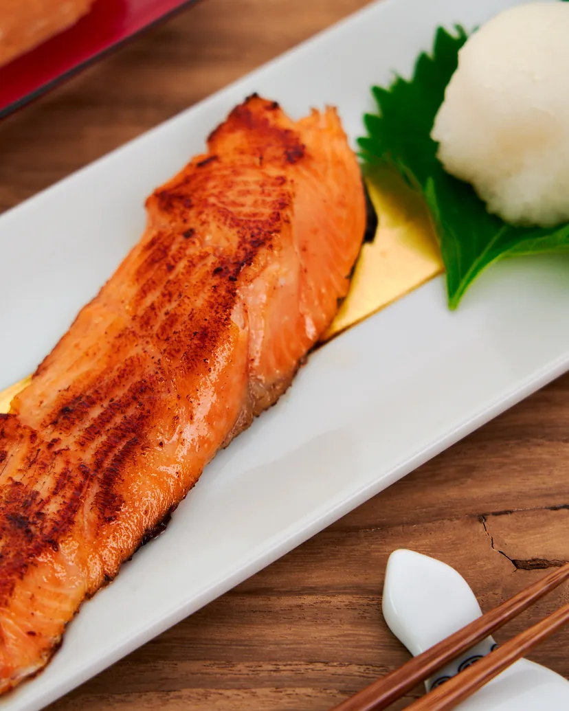 A grilled salted salmon fillet on a white plate with grated daikon