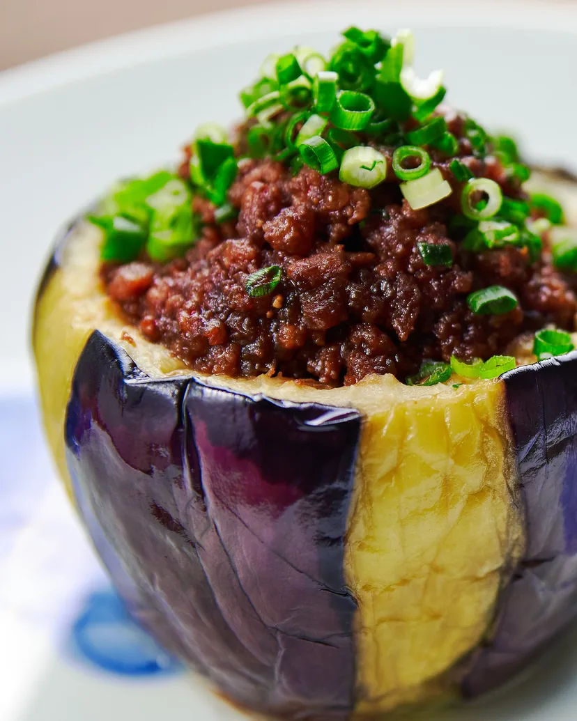 A hollowed eggplant filled with miso-glazed ground meat and topped with green onion
