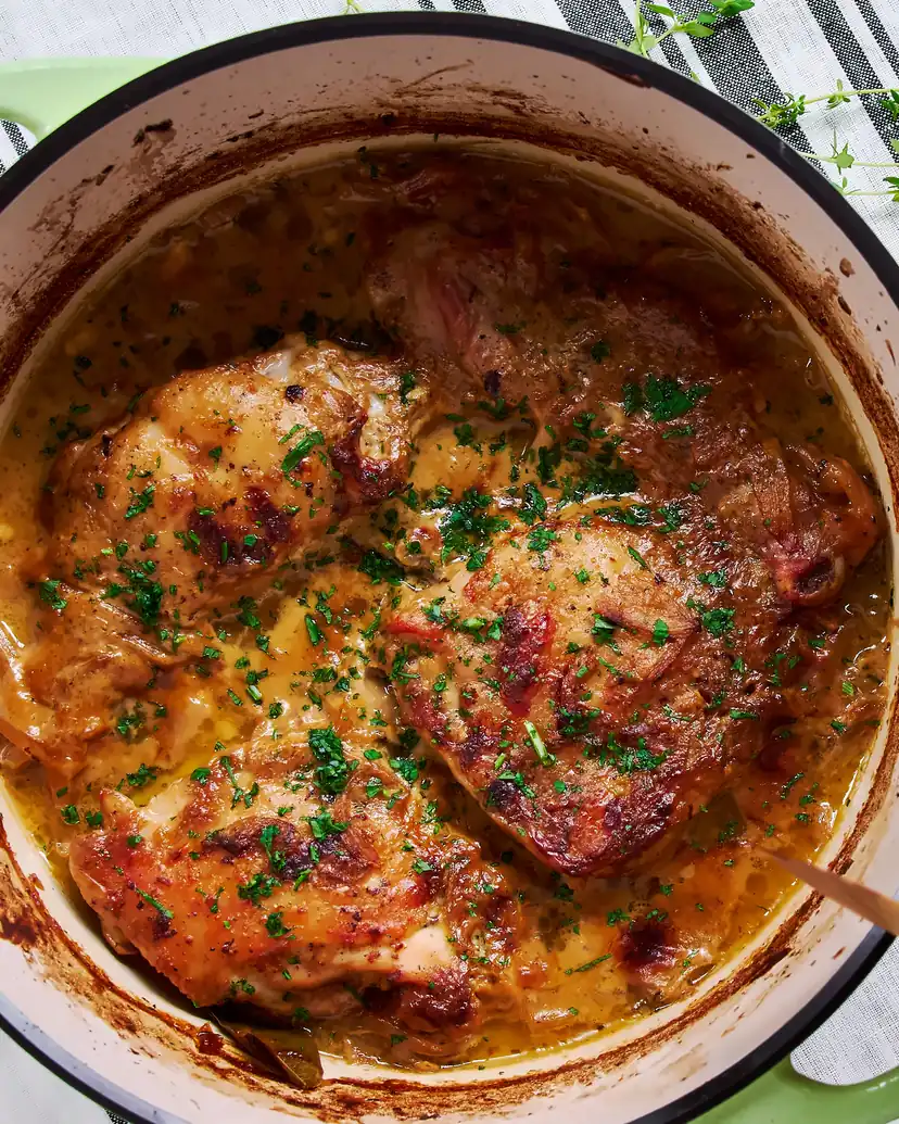 Browned chicken thighs in a creamy mustard sauce scattered with parsley, in a white enamelled pot