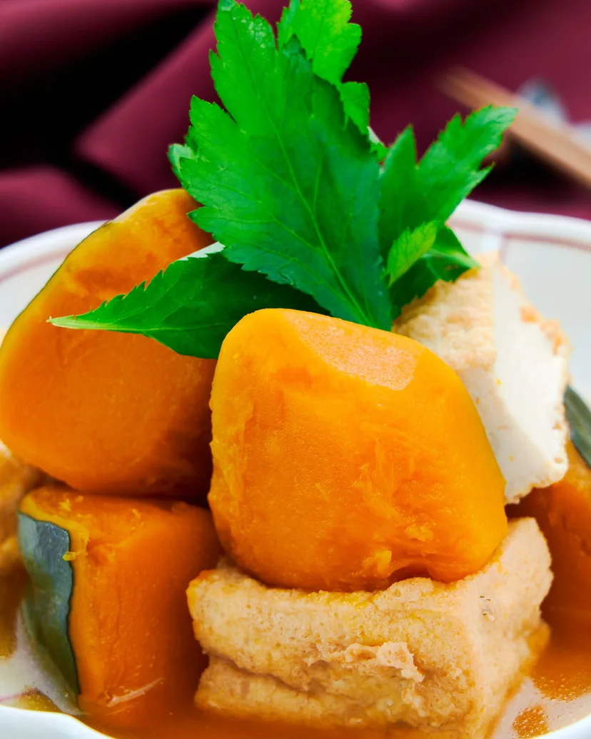 Simmered kabocha squash with fried tofu in dashi, garnished with mitsuba