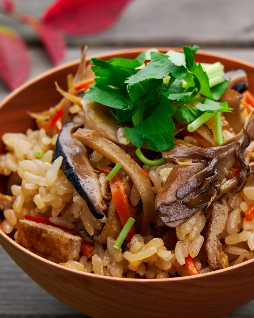 Mixed rice with mushrooms, carrot and fried tofu, topped with mitsuba, in a wooden bowl
