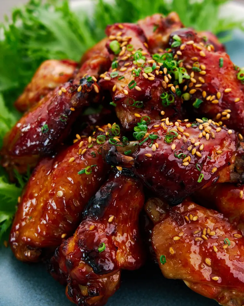 Sticky glazed teriyaki chicken wings with sesame seeds and green onion on a bed of greens