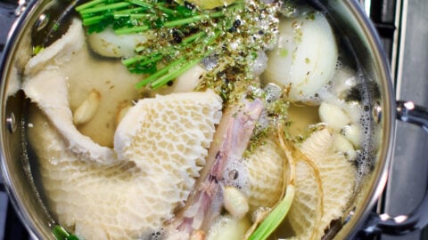 Tripe with pig trotters, aromatics, and herbs in a pot of water.
