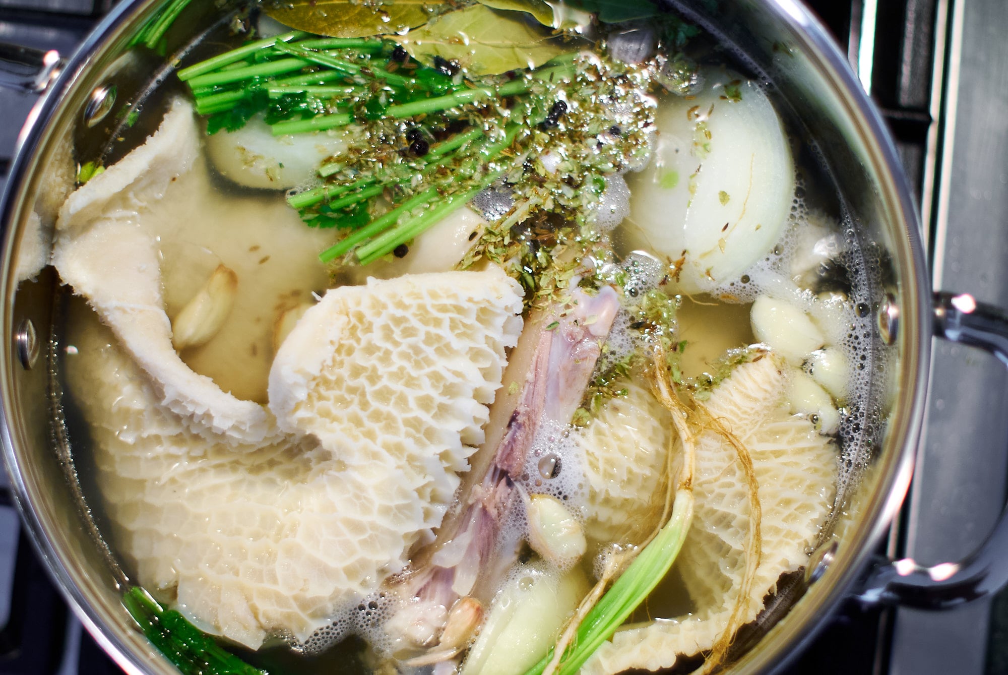 Tripe with pig trotters, aromatics, and herbs in a pot of water.