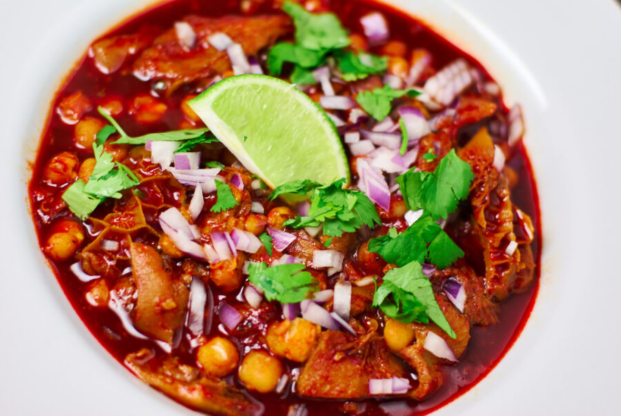 A vibrant tripe and pig trottter Menudo topped with red onions, cilantro and lime.