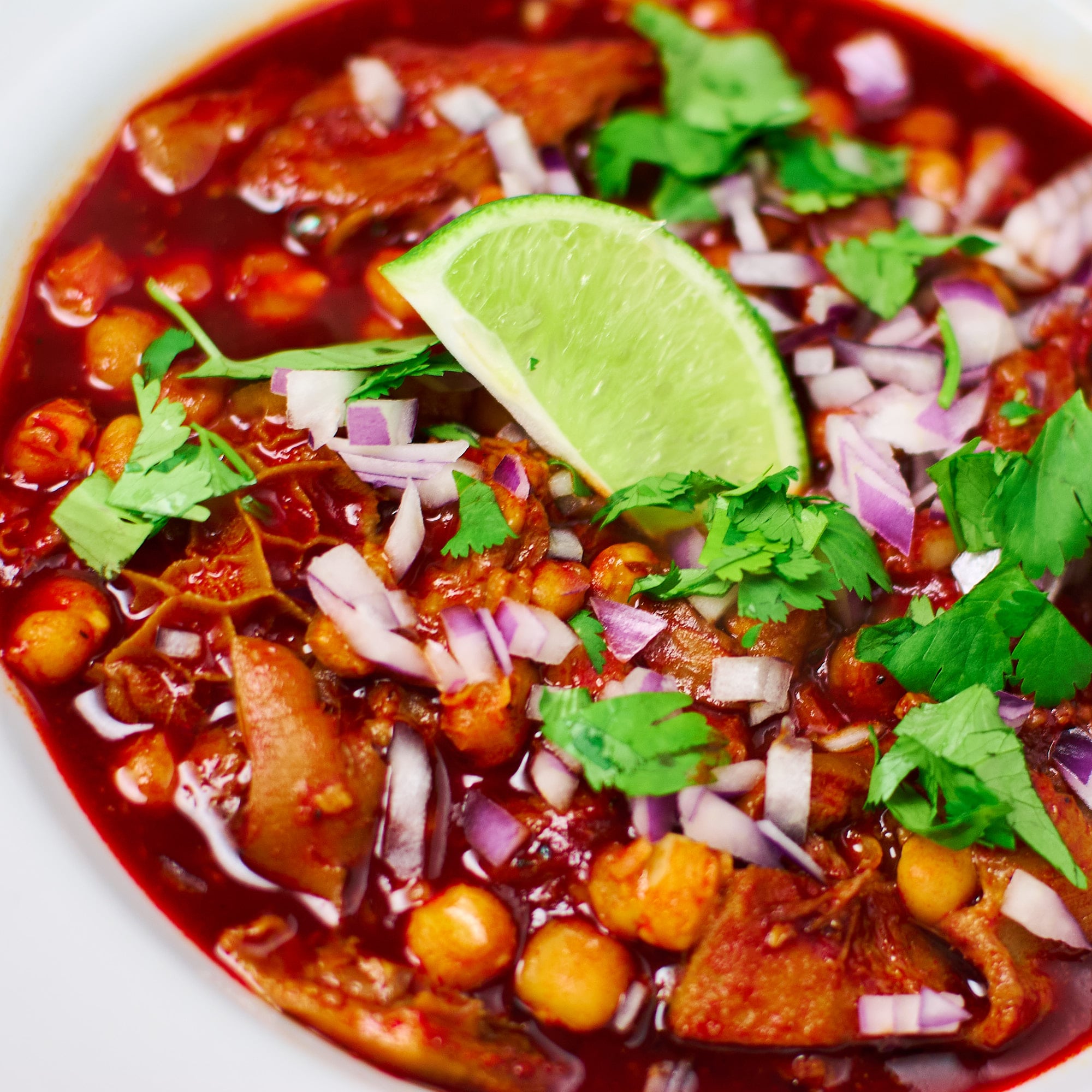 A vibrant tripe and pig trottter Menudo topped with red onions, cilantro and lime.