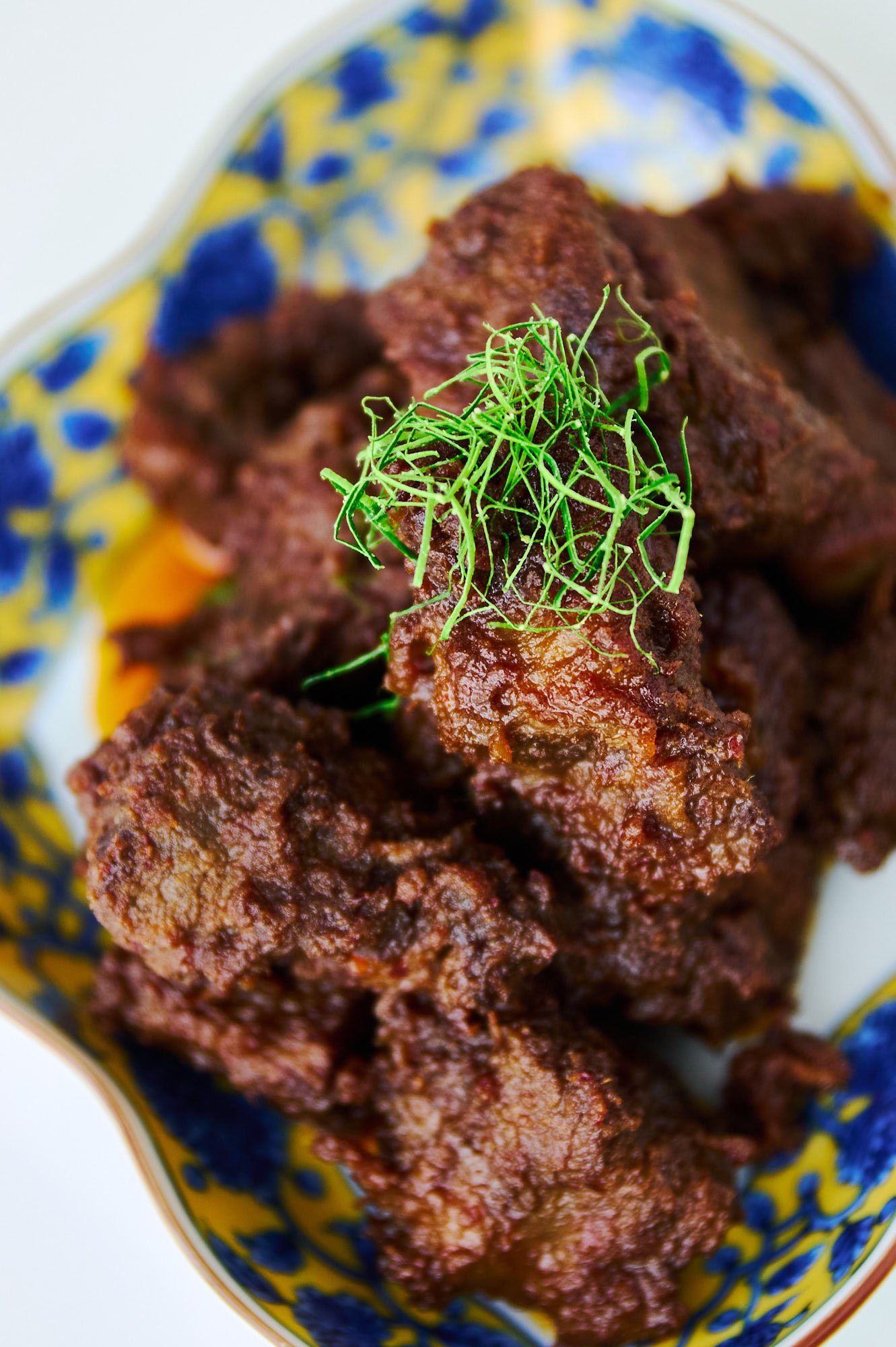 A plate of glistening Beef Rendang showcases its rich coating of caramelized spices and aromatics wrapped around fall apart tender chunks of beef.