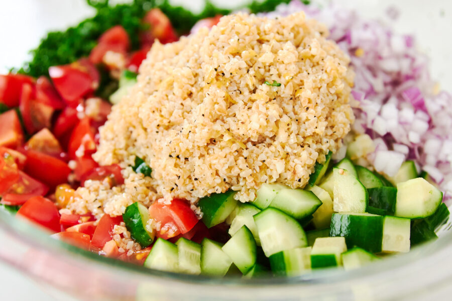 A glass bowl brims with neat quadrants of chopped parsley, juicy tomato, cool cucumber, minced red onion, and a generous mound of fluffy bulgur, poised to be tossed into vibrant tabbouleh.