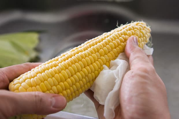 Rubbing ears of fresh corn to remove silks.