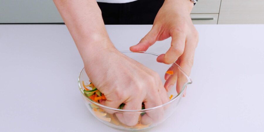 Squeezing carrots and cucumbers to remove excess water.