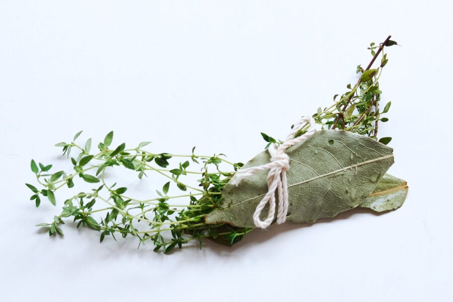 A fragrant bundle of bay leaves and thyme, tied with twine, waits to perfume the mustard‑braised chicken with fresh, herbal depth.