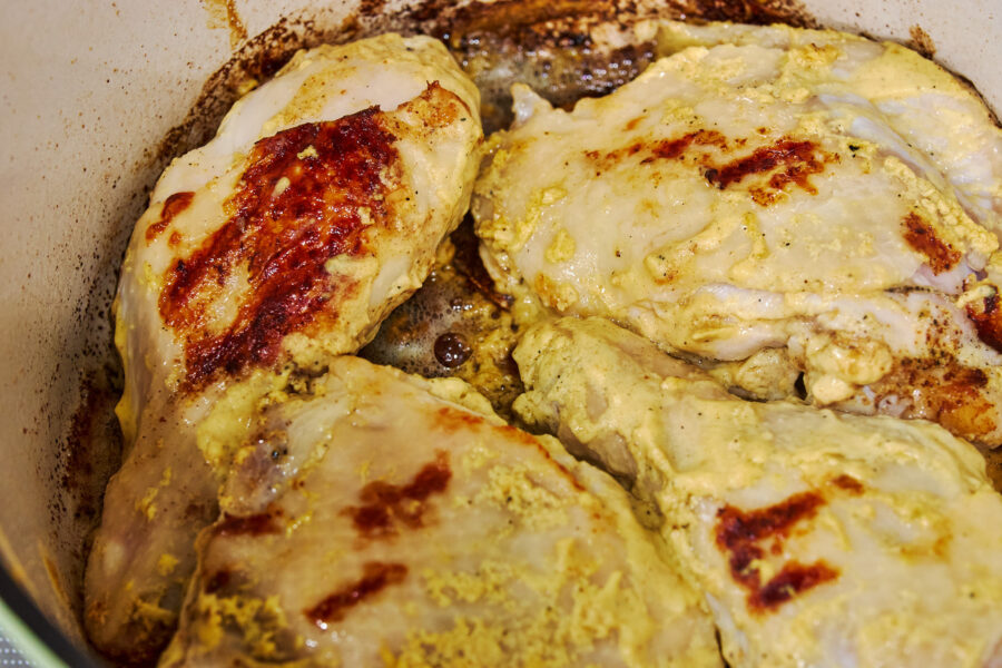 Mustard‑coated chicken sizzles in a Dutch oven, its skin blistering to a golden crust that crackles with savory aromas.