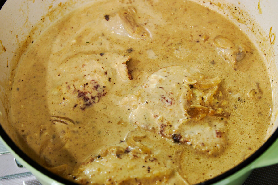 Chicken pieces braise in a creamy Dijon mustard sauce, the surface flecked with spices and glistening with richness.