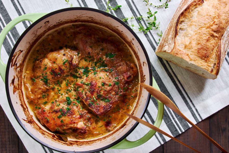 An overhead view showcases bronzed chicken thighs bathing in glossy mustard gravy, steam curling up to invite a hearty spoonful.