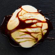 A silky dome of vanilla-specked vegan panna cotta draped with glossy black sugar syrup, artfully served on a slate plate.