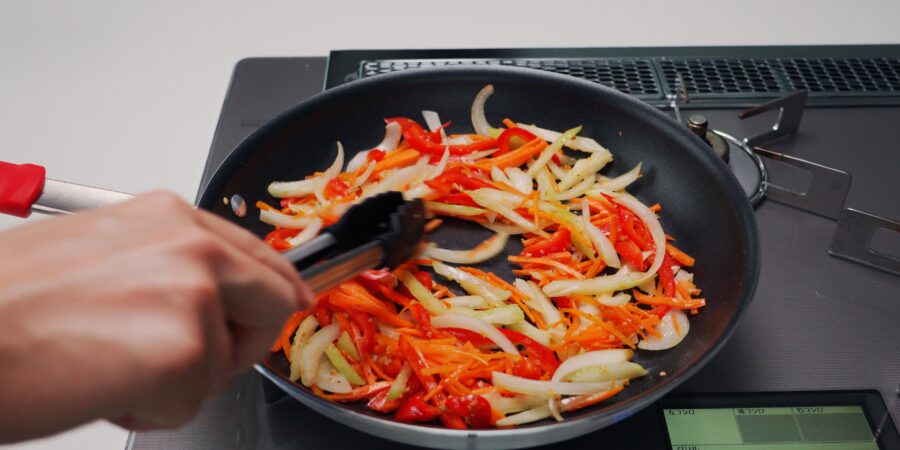 Stir-frying carrots, celery, onions and bell peppers in a frying pan.