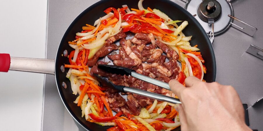 Browning marinated pork in a frying pan with vegetables for making Chop Suey.