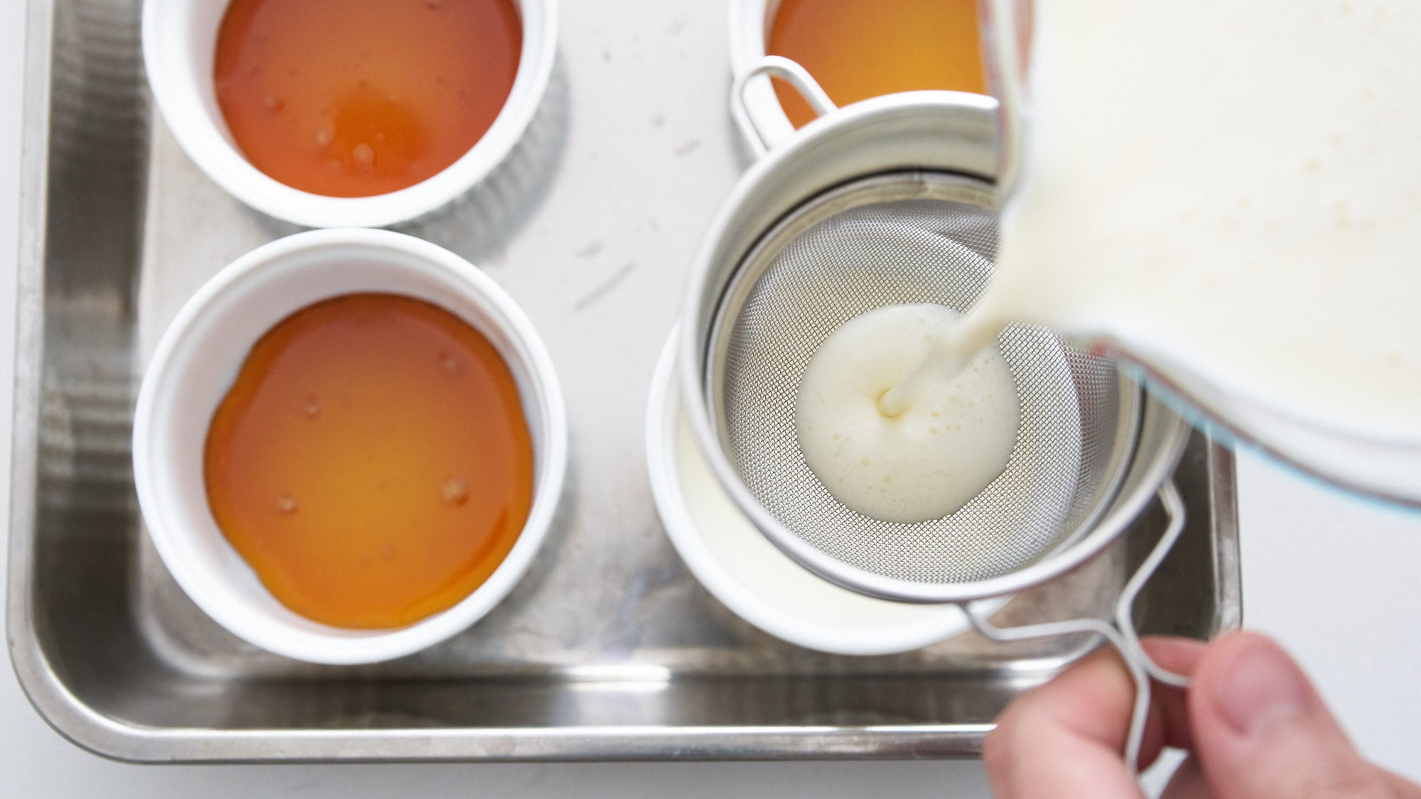 Straining panna cotta custard mixture into ramekins lined with caramel.