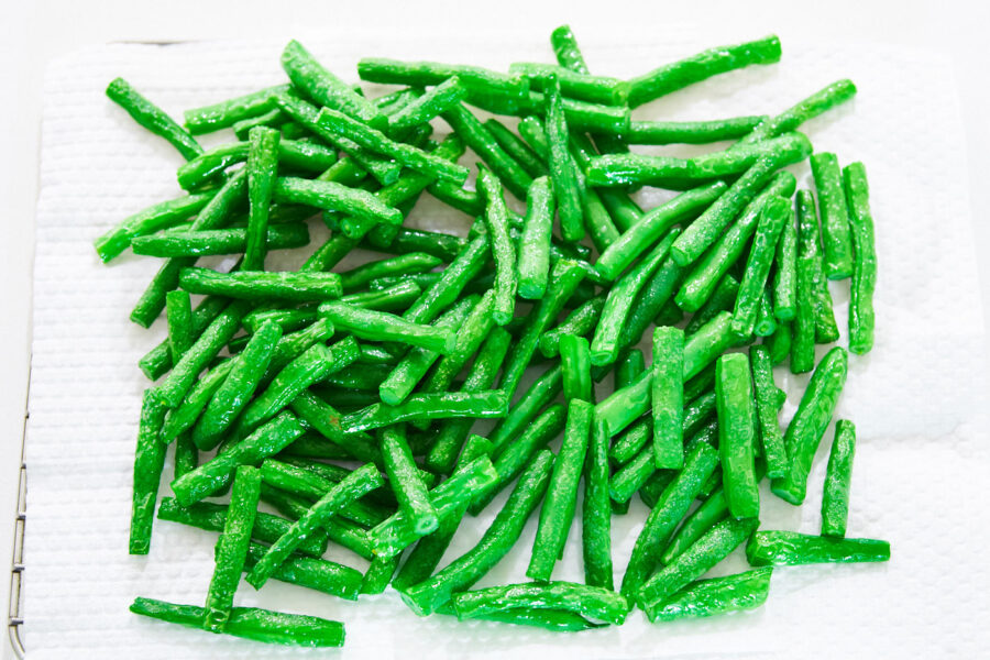 Oil-blanched green beans draining on paper towels before being stir-fried with black bean sauce.