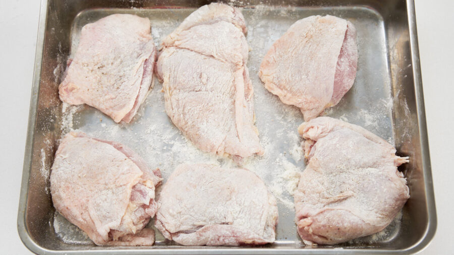 Chicken thighs dusted with flour on a tray for making honey lemon chicken.