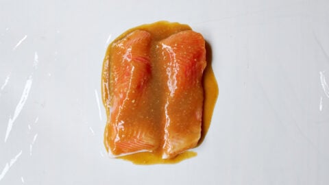 Salmon fillets coated evenly with miso paste on plastic-wrapped surface before wrapping.