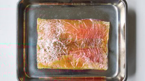 Salmon fillet nestled on a small metal tray, fully wrapped in miso marinade to cure.