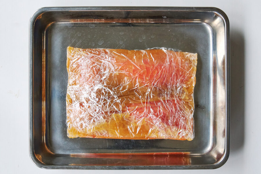 Salmon fillet nestled on a small metal tray, fully wrapped in miso marinade to cure.