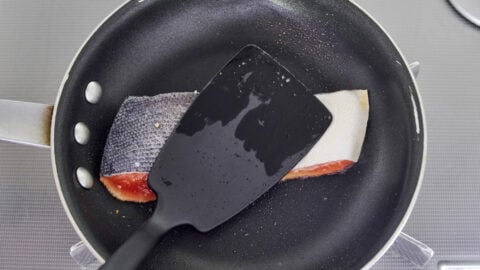 Salmon in a nonstick skillet being pressed with a spatula to brown evenly.