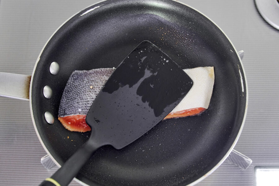 Salmon in a nonstick skillet being pressed with a spatula to brown evenly.