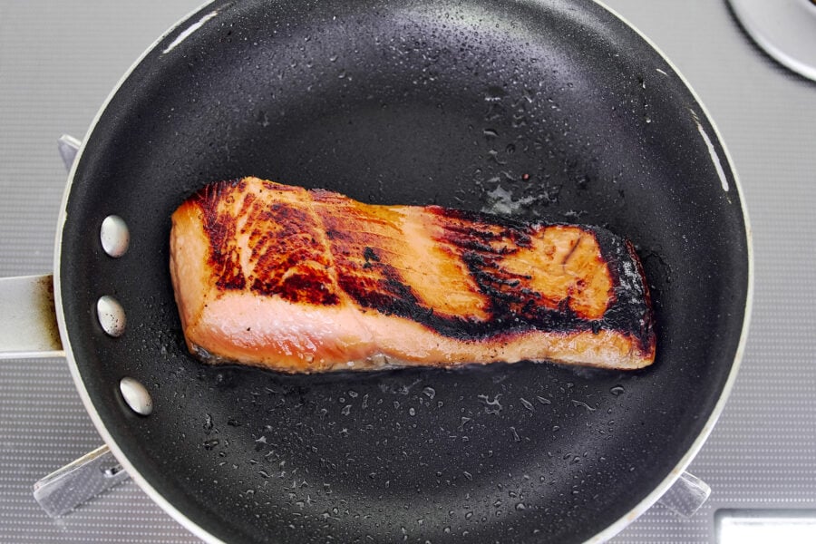 Salmon flesh-side down in a skillet, miso glaze caramelized to a deep golden color.