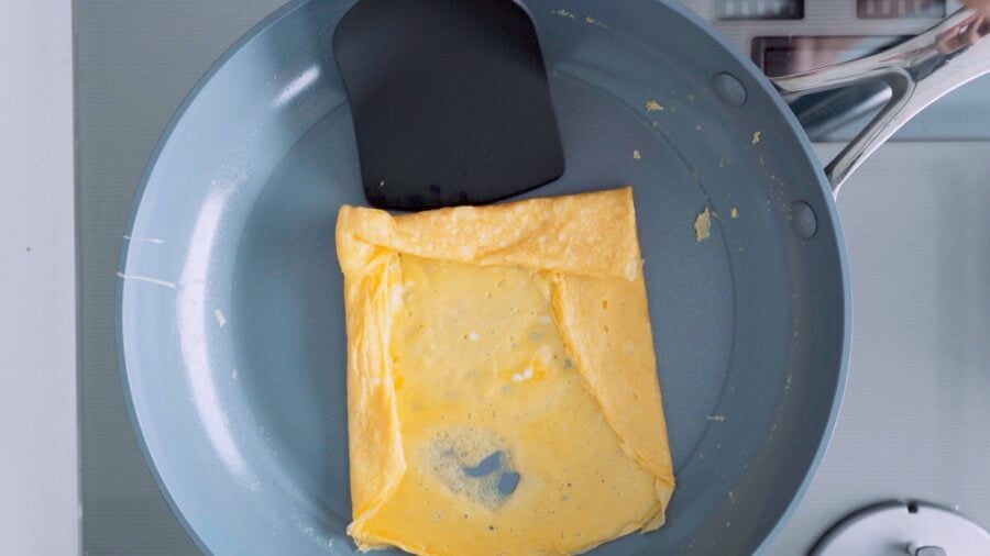 Layer of egg in a round frying pan being rolled up for Tamagoyaki.