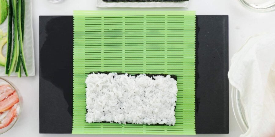 Rice evenly spread across nori for uramaki style sushi roll.