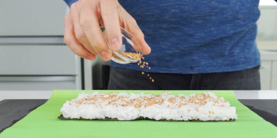 Sprinkling toasted sesame seeds onto sushi rice.