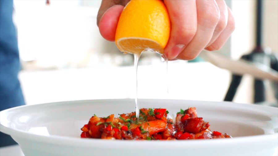 Squeezing a half lemon onto a bowl of shrimp and grits.
