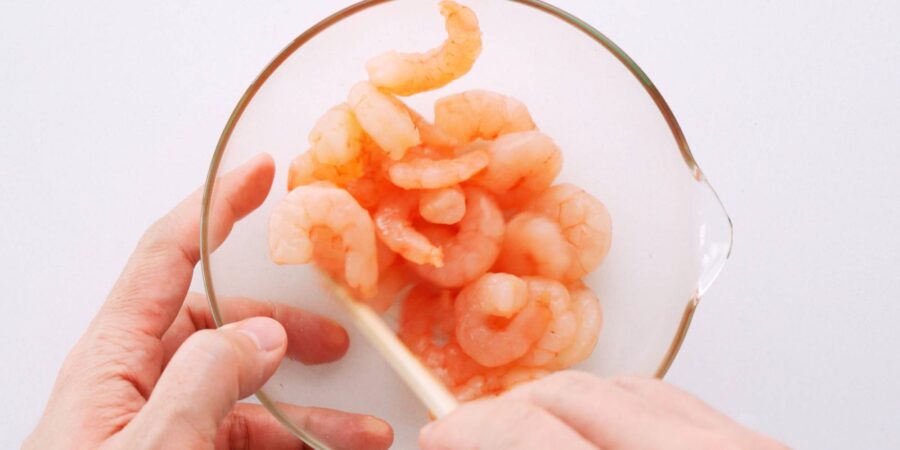 Marinating small pink shrimp in a glass bowl.