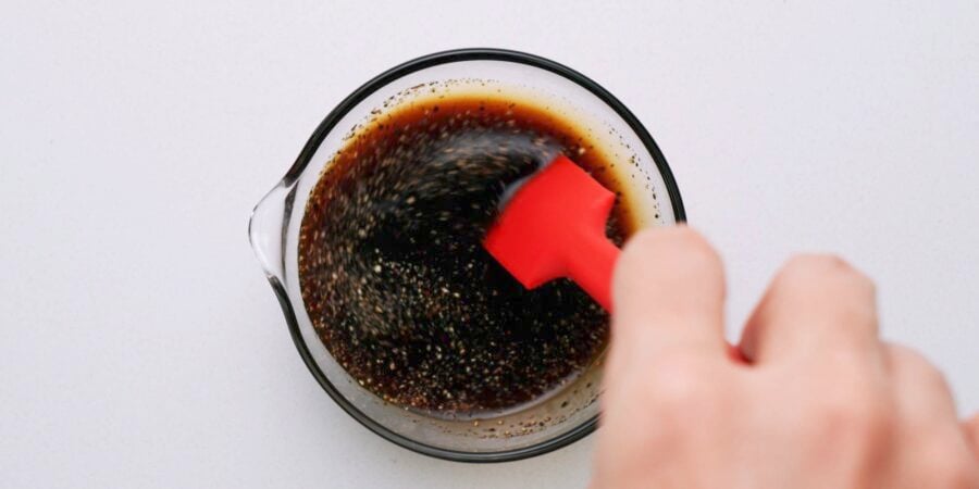 Stirring Yaki Udon sauce with a red spatula in a glass bowl.