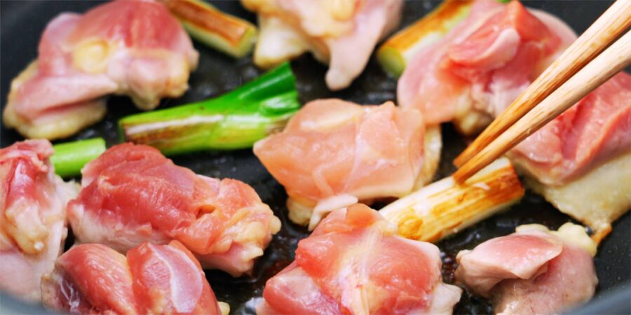 Chicken and scallions grilling in a pan.