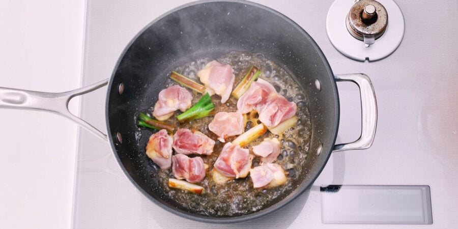 Chicken and scallions in a pan being deglazed with sake.