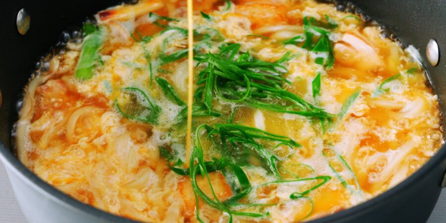 Drizzling egg into chicken udon noodles.