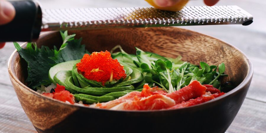 Grating yuzu zest onto a California Roll sushi bowl.