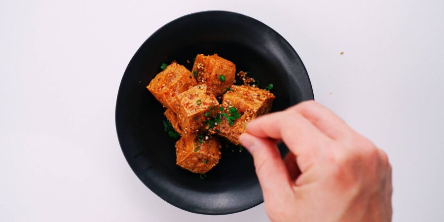 Garnishing crispy tofu bites with scallions.
