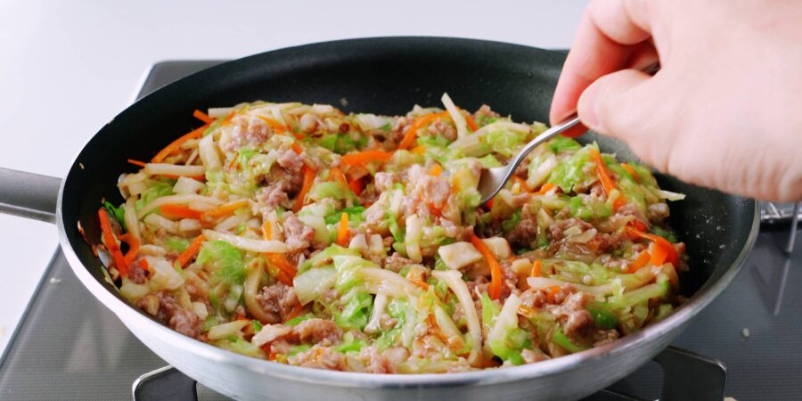 Tasting Japanese spring roll filling from a frying pan.
