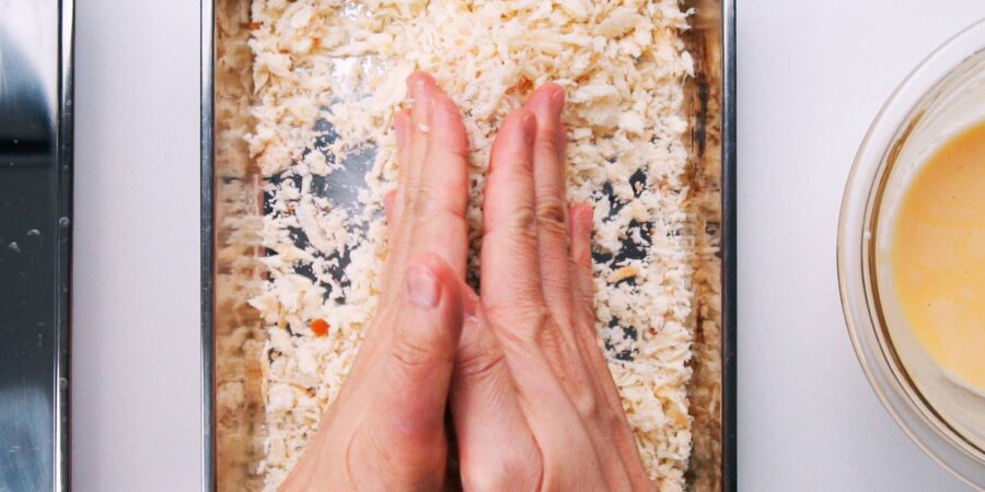 Pressing panko onto shrimp with hands.