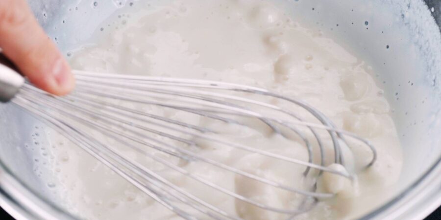Whisking partially cooked mochi in a glass bowl.