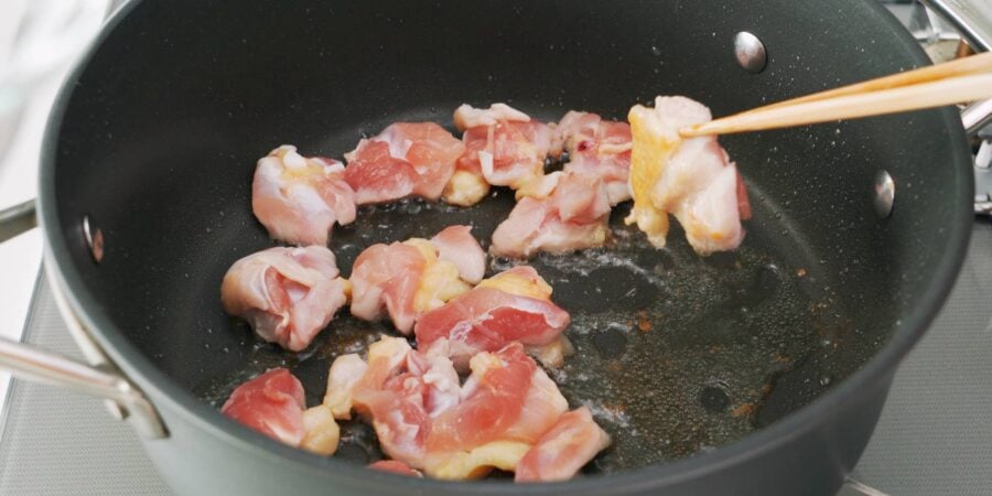 Browning chicken thighs in a frying pan for curry udon.